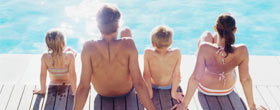 Family sitting on decking by a pool.