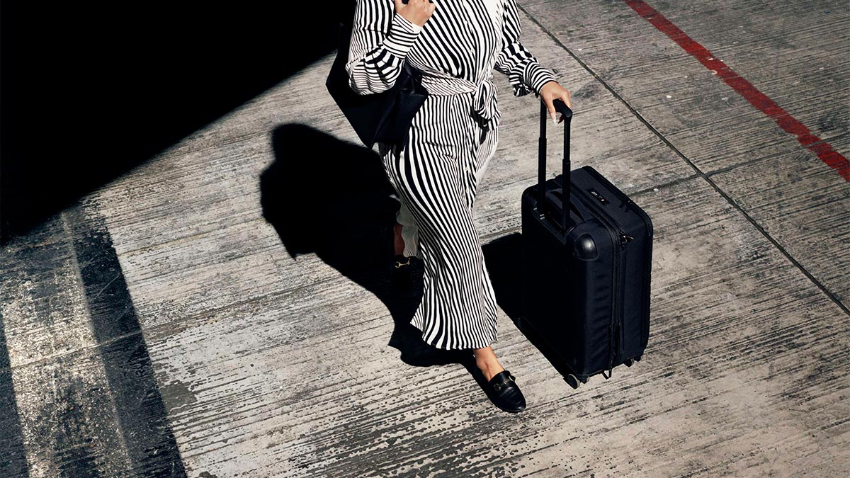 Female traveller with trolley suitcase, viewed from a high angle with shadow.