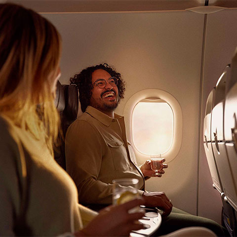 A male passenger sat in a Club Europe cabin, laughing while holding a drink next to a female passenger.