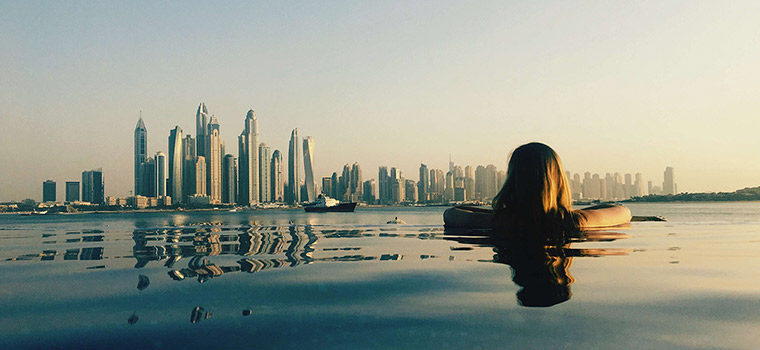 Girl in pool looking at Dubai cityscape.