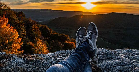 Una persona sentada en una montaña viendo una puesta de sol.