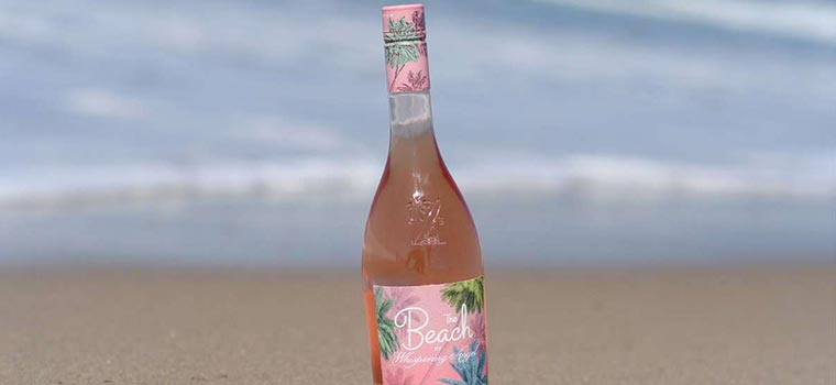 Bottle of Whispering Angel 'The Beach' on the shore of the beach, with the tide encompassing the bottom of the bottle.