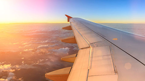Vista aérea de um avião que voa por cima das nuvens durante o por do sol. Vista da janela do avião num momento emotivo durante uma viagem internacional à volta do mundo.