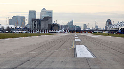 Pista no aeroporto de London City com os arranha-céus de Londres ao fundo.
