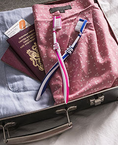 Open suitcase on bed with UK passports and pink and blue toothbrushes.
