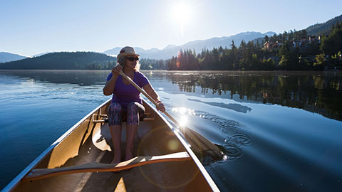 Senior aged woman canoeing on a pristine lake at sunrise.
