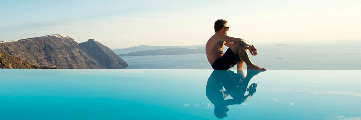 Uomo seduto sul bordo di piscina a sfioro a Santorini, Grecia.