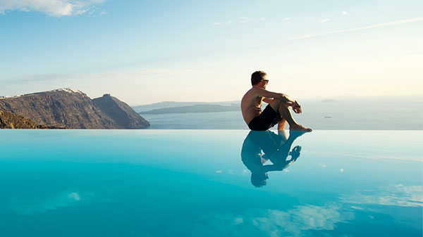 Uomo seduto sul bordo di una piscina a sfioro a Santorini, Grecia.