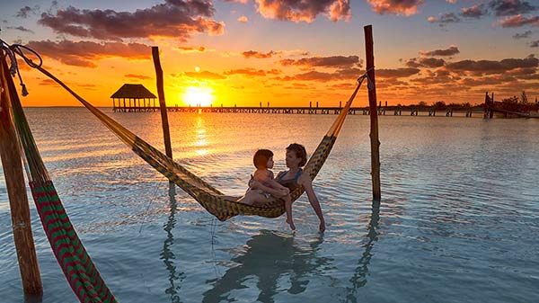 Mother and child relaxing on a hammock during sunset.