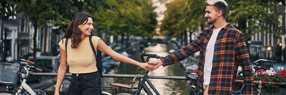 Two people holding hands on bridge over Amsterdam river.