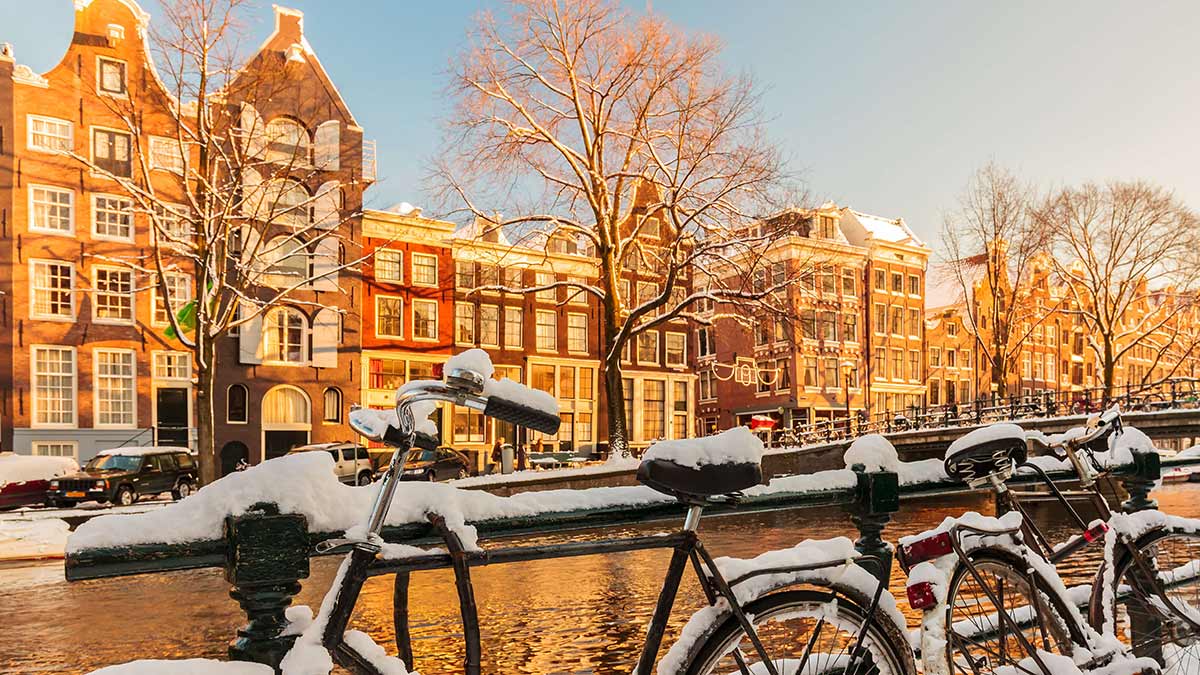 Bicycles covered with snow alongside a canal during winter in Amsterdam