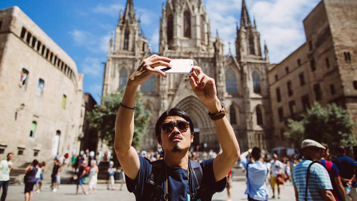 Young Asian man taking a selfie in front of the Barcelona Cathedral in Spain.