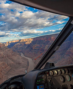 An aerial view of the Grand Canyon. Shadows are being cast over the Grand Canyon landscape contrasted against the blue sky just before the sun sets. Photographed with a wide angle lens and the helicopter control panel and window frame is visible.