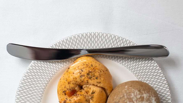 Pãezinhos e faca de manteiga pousada no serviço de porcelana, disponíveis em First.