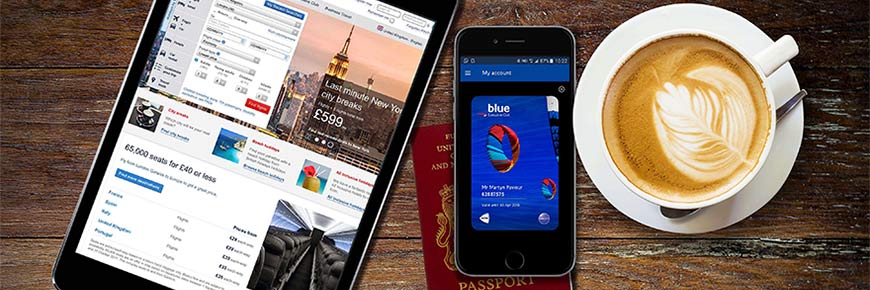 Планшет и мобильный телефон с открытой страницей ba.com, лежащие поверх паспорта рядом с чашкой кофе.