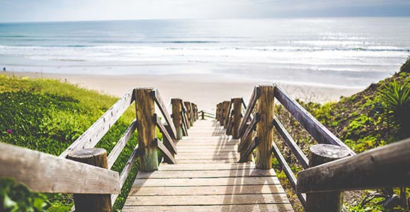 Escalerilla que une un paseo marítimo con una playa soleada.