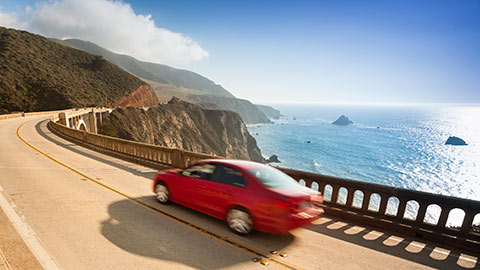 Red car driving along a coastal road.