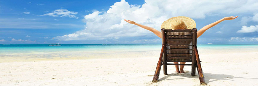 Woman sitting on a chair on a sandy beach in the sun.