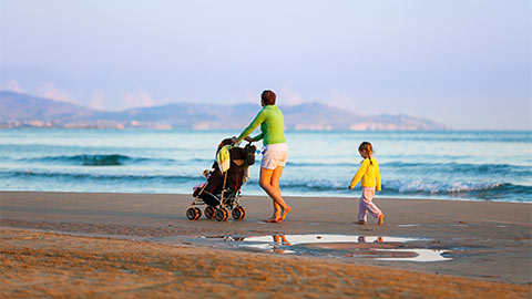 Woman and child on a beach with a pushchair.
