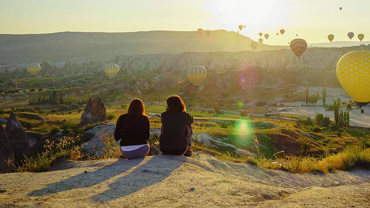 Frauen, die Heißluftballone bei Cappadocia auf einem Berg sitzend betrachten.
