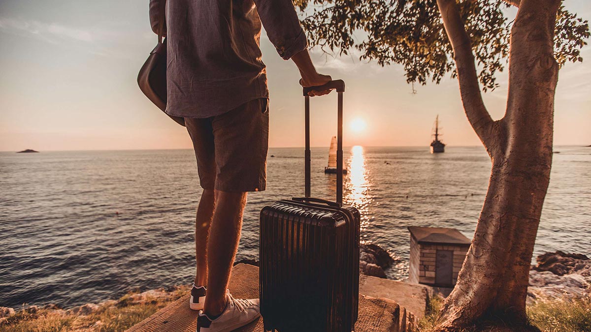 Moderno gentleman turista con valigia in riva al mare.