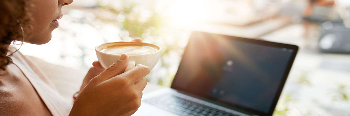 Imagem recortada de mulher a beber café com um computador portátil à mesa de um restaurante. Jovem num café a segurar uma chávena de café.