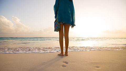 Girl standing on beach at sunset, Barbados, Caribbean.