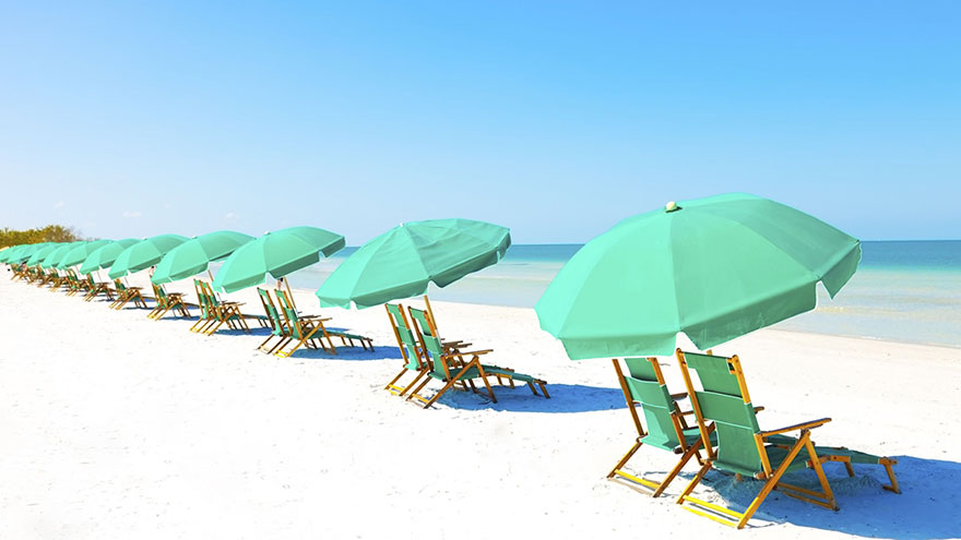 Green beach loungers and umbrellas at white sandy beach.
