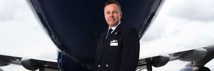机长 Steve Allright 身着制服，站在一架飞机下。